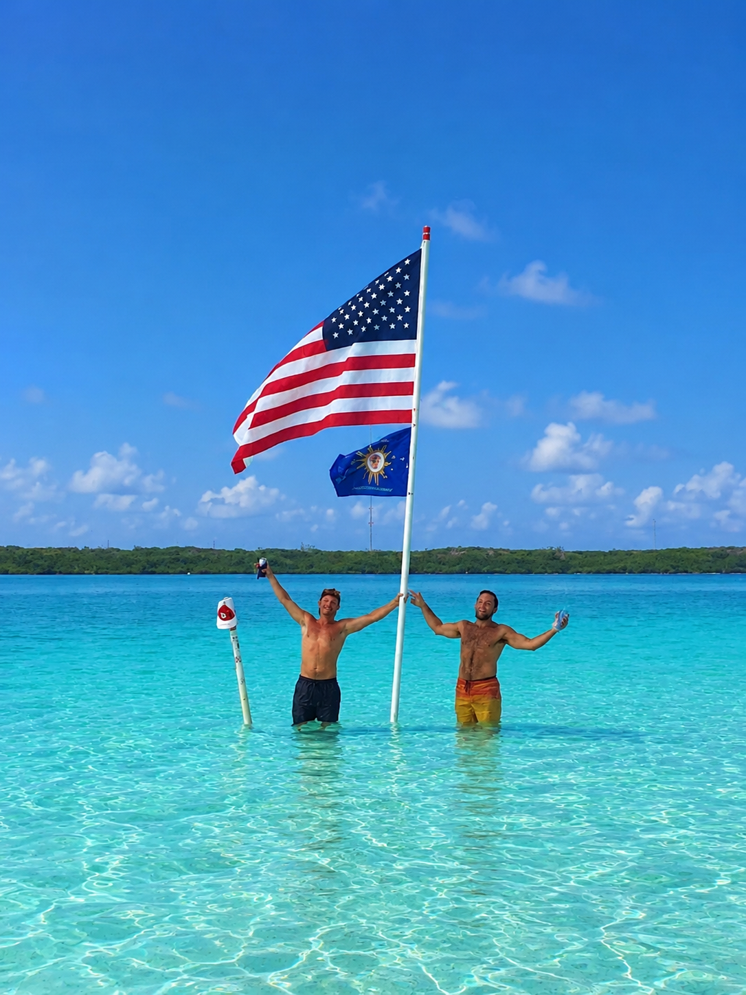 Two people standing on a sandbar with an American flag