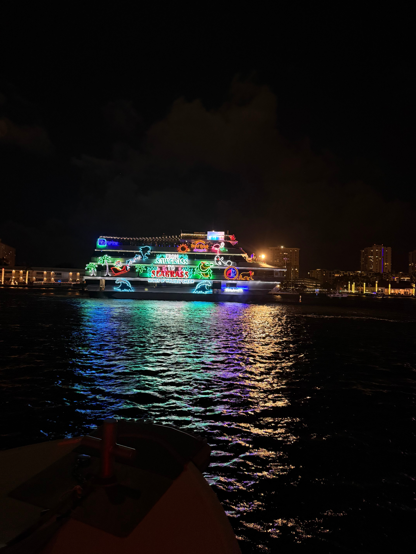 Holiday-lit boat reflecting neon colors on the water at night